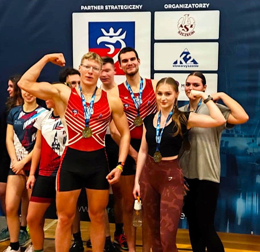 Studenci na zdjęciu z medalami pozują do zdjęcia pokazując mięśnie